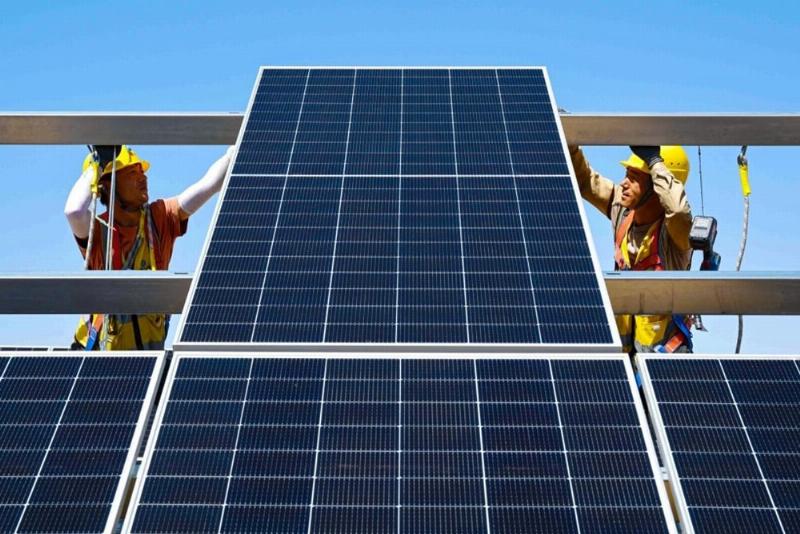 Một chiếc xe điện VinFast đang sạc tại một trạm sạc có biểu tượng hoặc gần các tấm pin mặt trời/tuabin gió. Minh họa sự kết nối giữa xe điện và năng lượng sạch.